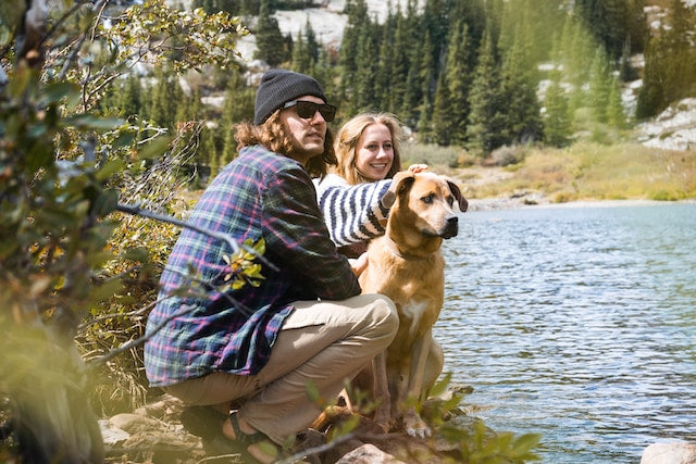 Happy couple in a purple and white striped long-sleeve shirt sitting beside their brown short-coated dog in a park.